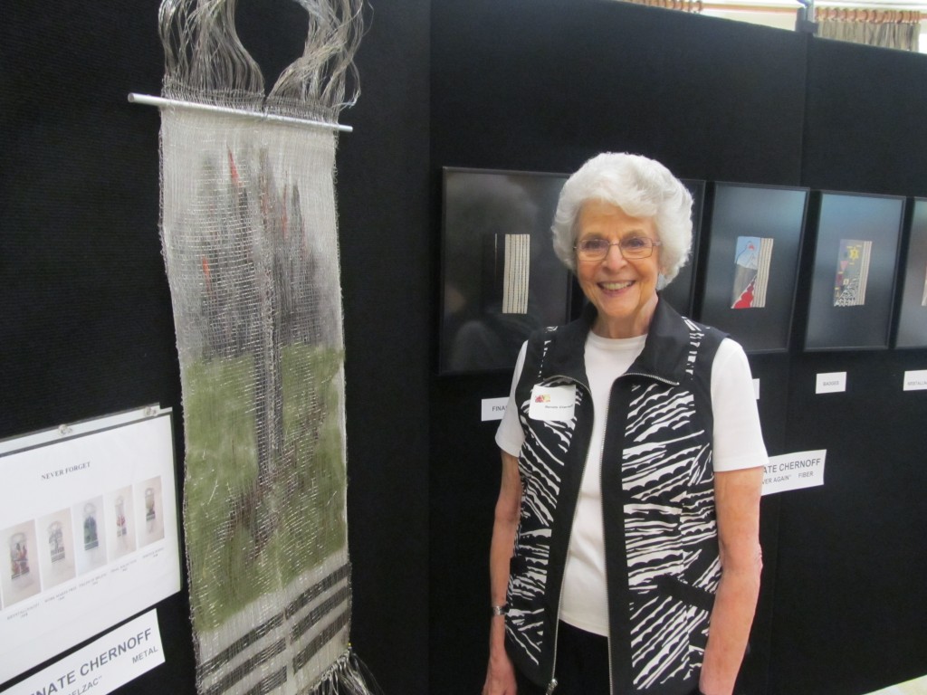Renate Chernoff, a resident of Riderwood retirement community in Silver Spring, is photographed with her metal weavings in a display titled “Never Again.” The six-panel series of titled tapestries portrays her personal feelings about the tragic events of the Holocaust that she witnessed as a girl from Breslau in the 1930s. The works of Mrs. Chernoff were part of A Feast for the Eyes III, a showcase of original artwork created by residents and staff of Riderwood held July 22-24. Photo courtesy of Riderwood retirement community